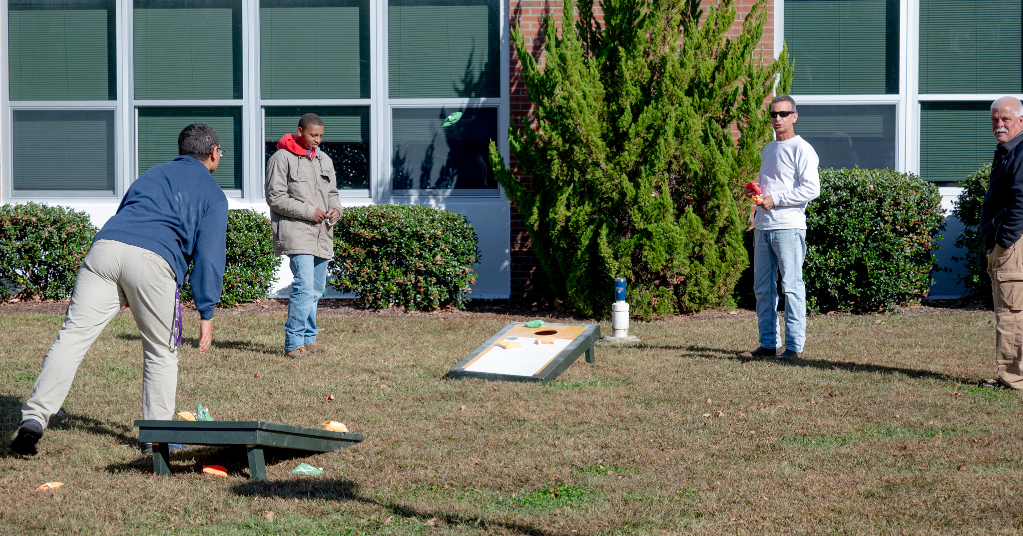 Ron, Curtis, and Chris look on as a student throws a bean bag at a corn hole board