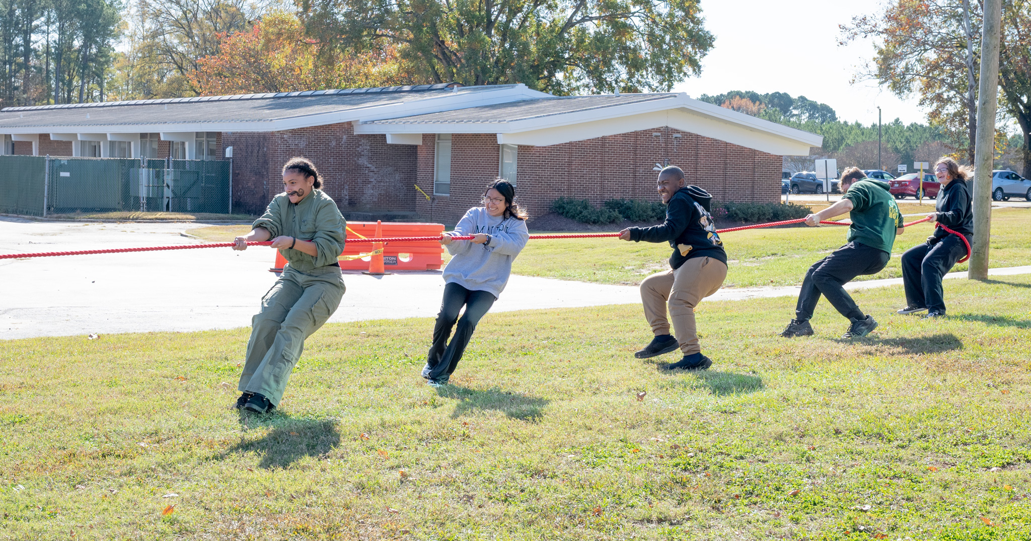 Fall Fest: 5 students tug one side of the rope in tug-of-war, a female student has a wonderful, face painted, mustache