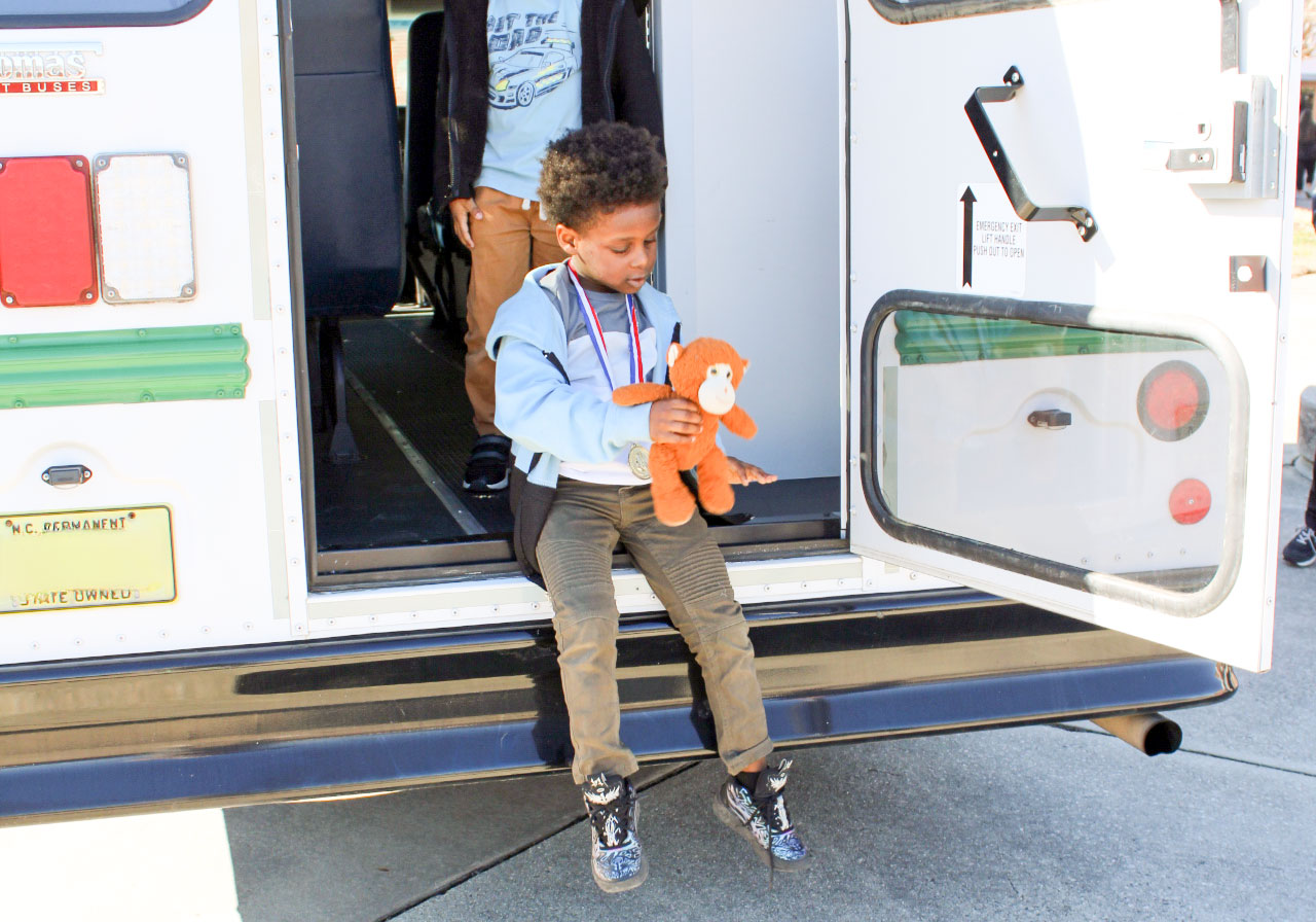 Student with stuffed monkey getting out of the back of a bus